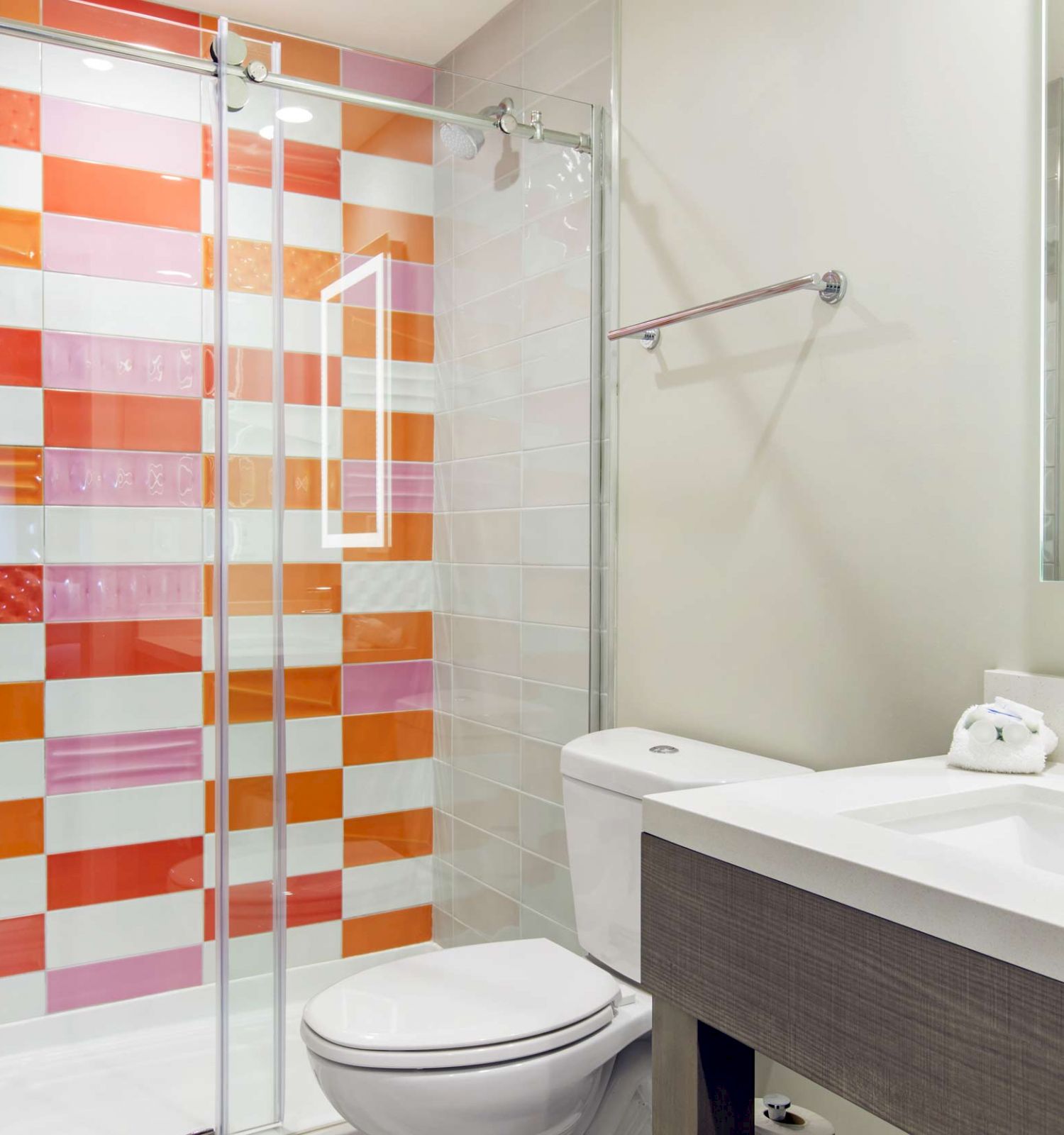 This image shows a modern bathroom with a shower, toilet, and sink. The shower has a glass door and colorful tiles in red and orange patterns.