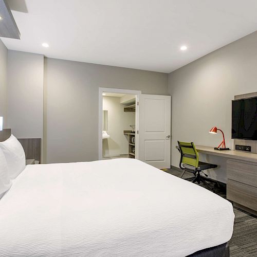 Modern hotel room with a large bed, TV, desk, chair, and open closet area with a bathroom visible through the door.