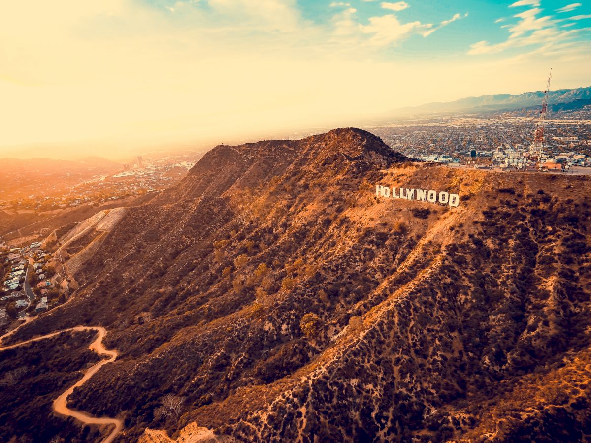 This image shows the famous Hollywood sign on a hill in Los Angeles, California, surrounded by a scenic landscape during sunset.