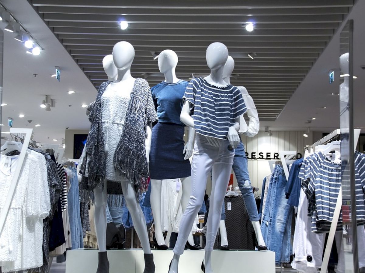 This image shows mannequins displaying outfits in a modern retail clothing store with bright lighting and various clothing items displayed.