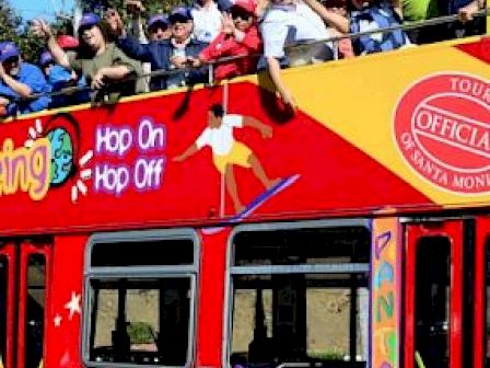 A crowded, vibrant double-decker red tour bus with people on the top deck, labeled 