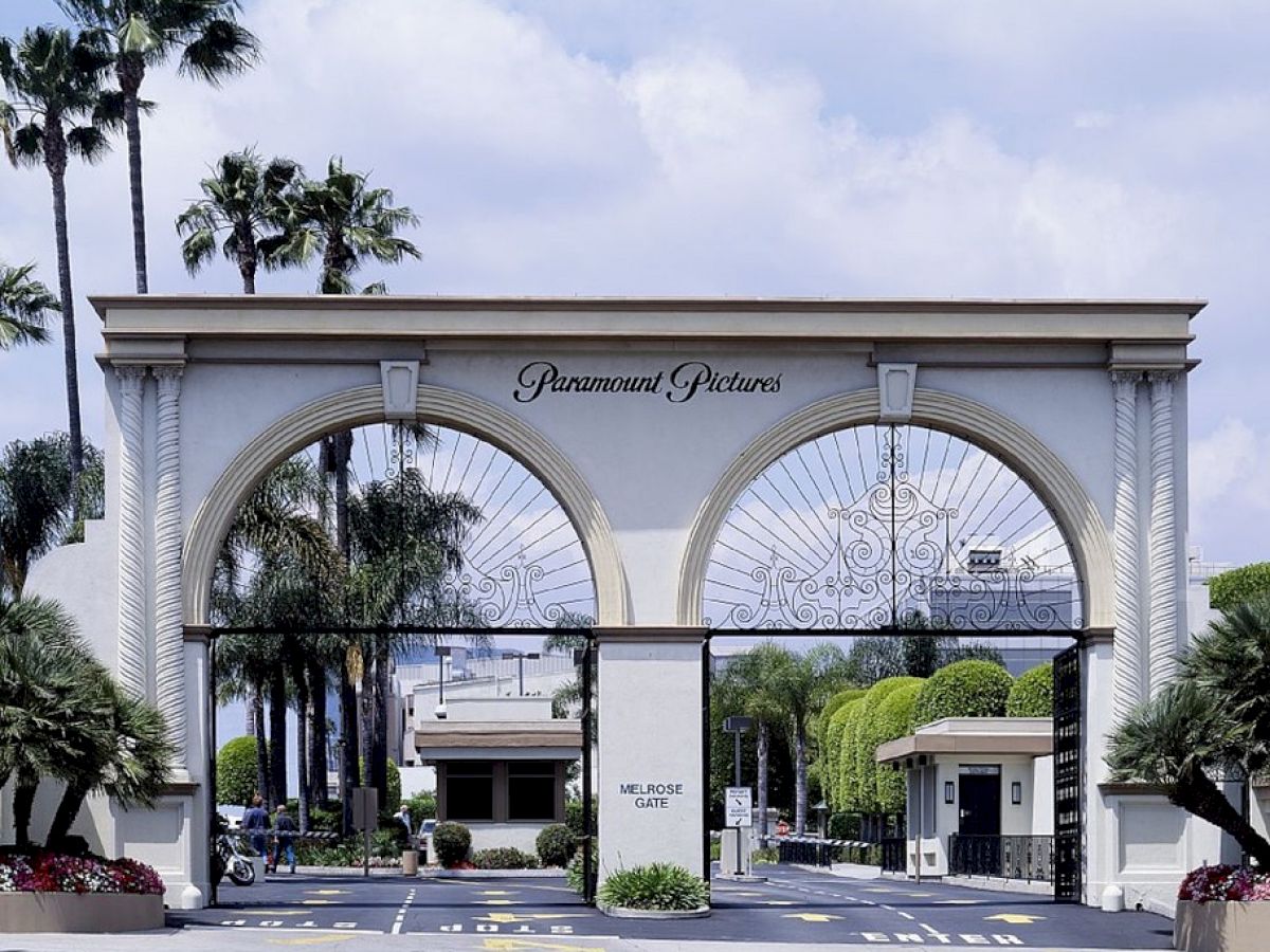 The image shows the entrance gate to Paramount Pictures, a historic film studio, adorned with arched gates and surrounded by palm trees.