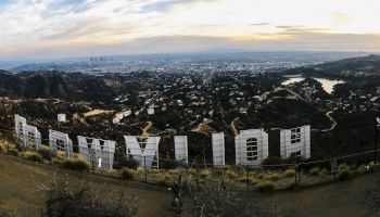 A panoramic view of the Hollywood Hills in Los Angeles, showcasing the city's iconic Hollywood Sign from behind, with the sprawling cityscape visible.