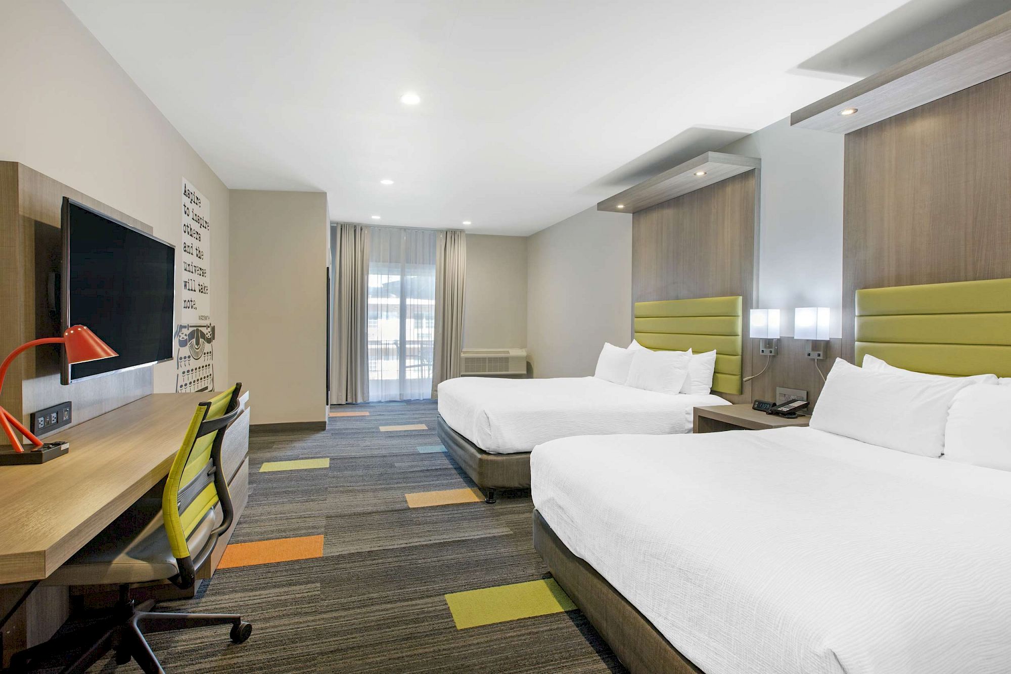 The image shows a modern hotel room with two queen beds, a desk, a red lamp, a chair, a TV mounted on the wall, and large windows with curtains.