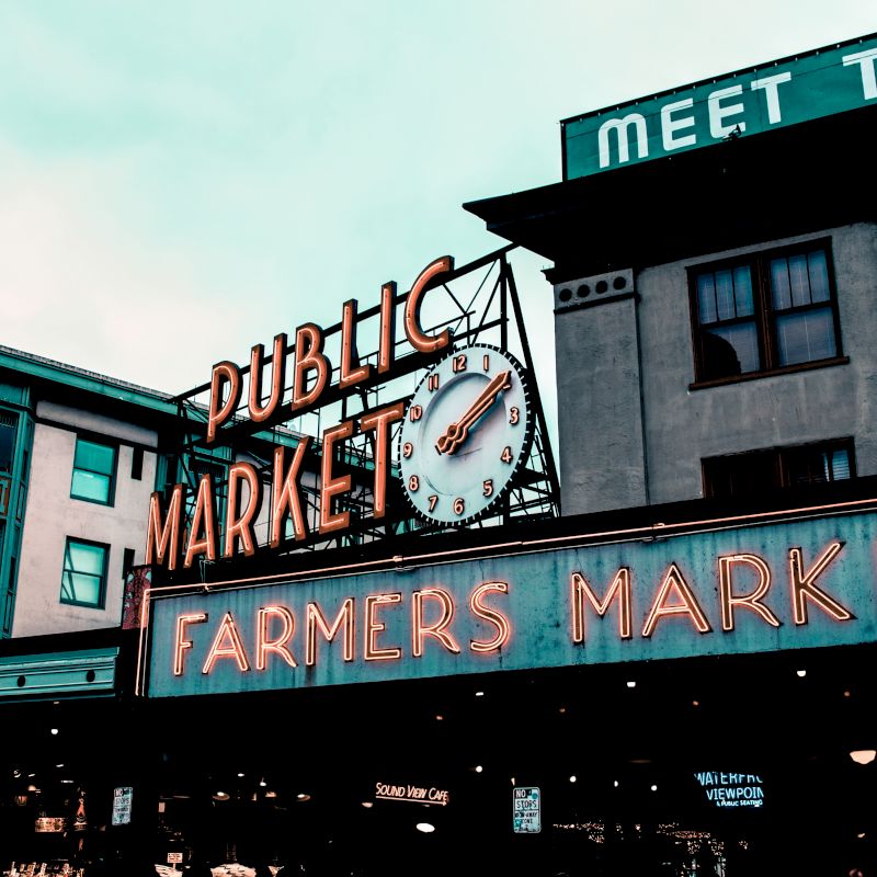 This image shows the famous Public Market Center sign at Pike Place Market in Seattle. The neon signs read "Public Market" and "Farmers Market."