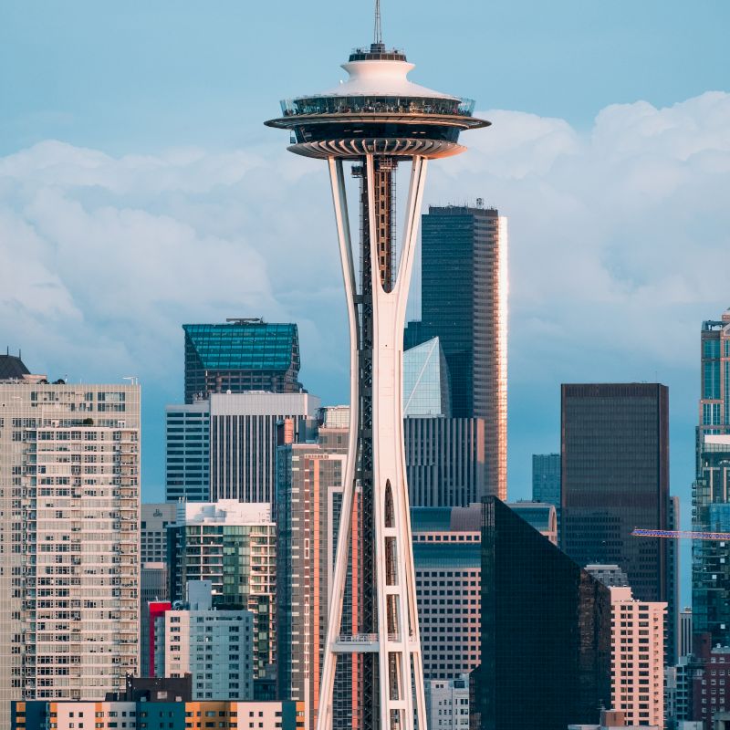 The image shows the Space Needle, a famous observation tower in Seattle, with the city's skyline and various buildings in the background.