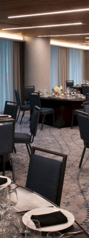 A banquet hall with round tables set for an event, featuring elegant table settings, chairs, and modern lighting.