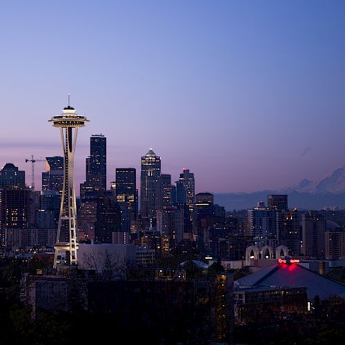 This image shows the Seattle skyline at dusk, featuring the Space Needle with Mount Rainier in the background, under a transitioning sky.