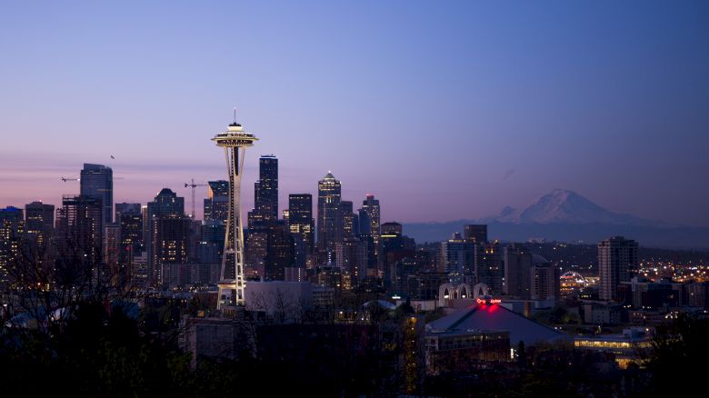 This image shows a cityscape at dusk with a prominent tower, tall buildings, and a mountain in the background under a purple sky.